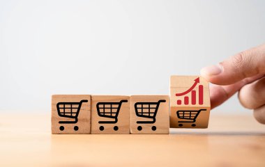 Hand flipping change between increasing graph and shopping cart trolley which print screen on wooden block cube for commerce business sales and order growth concept.