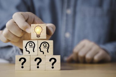Hand putting wooden cube block stacking which print screen glowing light bulb and question mark with human , Creative thinking idea and problem solving concept.