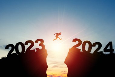 Mutlu Noeller ve mutlu yıllar 2024, Siluet Adam 2023 uçurumundan 2024 'e bulutlu gökyüzü ve güneş ışığıyla atlayan.