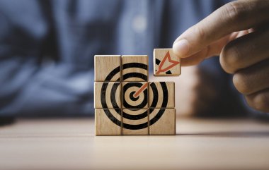 İş adamı hedef tahtası ve hedef kavramı oluşturmak için tahta küp bloğuna baskı yapan oklu hedef tahtası.