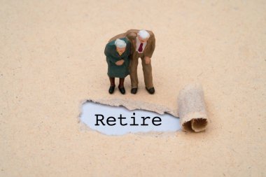 Birkaç minyatür figür. Emeklilik ikramiyesi, emeklilik sigortası, finansal planlama ve emeklilik sigortası için kahverengi punç kağıdına yazı yazarak emekli olan yaşlı adam ve kadın.. 