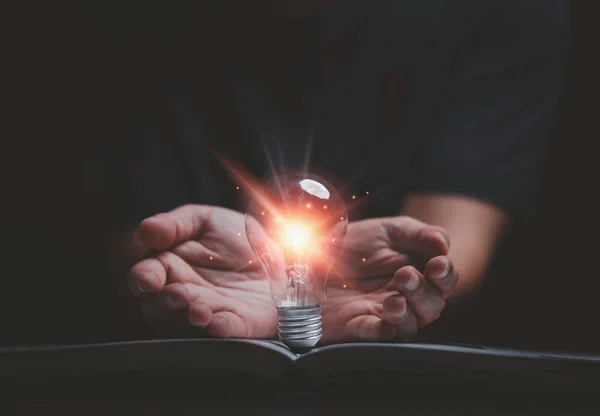 Hand giving glowing lightbulb on open book for creative thinking idea to solve problem from learning knowledge and innovation concept.