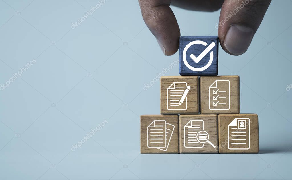 Hand holding white correct sign mark on blue wooden block cube and the top of document icon for ISO quality control certification and project approval concept.