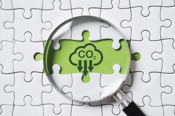 Magnifier glass with CO2 reduction on green background and jigsaw for decrease CO2 , carbon footprint and carbon credit to limit global warming from climate change in Kyoto Protocol 2050 concept.