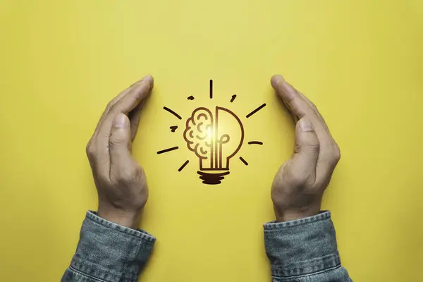 2つの手は黄色い背景の輝く電球を保護し 問題解決の特許そして考えおよび創造的な考えの概念を防ぎます ロイヤリティフリーのストック写真
