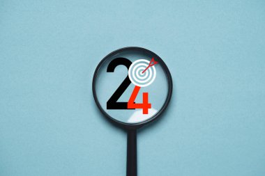 Hedefe odaklanmak için büyüteç içinde dart tahtasıyla geçirilen 2024 yılı iş, hayat, sağlık, aile kavramı.