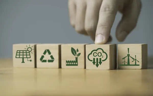 Hand pushing carbon reduction icon on wooden block cube among environmental ecology icon include green factory recycle windmill and solar cell for decrease CO2 , carbon footprint and carbon credit.