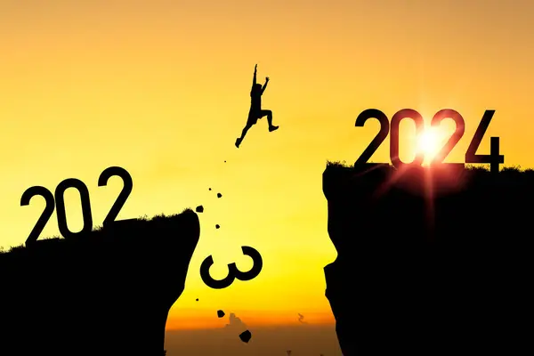 2024年にようこそメリークリスマスと幸せな新年 シルエットマンは2023崖から黄色い空と朝の日の光で2024崖にジャンプ ロイヤリティフリーのストック画像