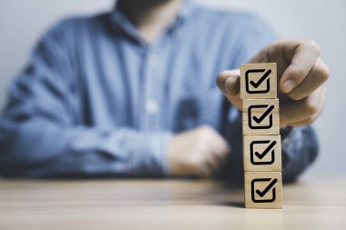 İşadamı, kalite güvencesi ve sürekli iyileştirme konsepti için tahta blok küpünün üzerine doğru işaret levhası istifliyor..