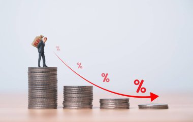 İşadamı minyatür figürü, tüketici yükü için azalan okla dolu bozuk paraların üzerinde büyük para çantası taşıyor veya ipotek krizi kavramını ödünç alıyor..