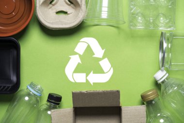 Çöplerle çevrili olan geri dönüşüm sembolünde, yeniden kullanım ve geri dönüşüm için plastik bir şişe, karton, plastik bir bardak ve çevresel sürdürülebilirlik kavramı yer alıyor..