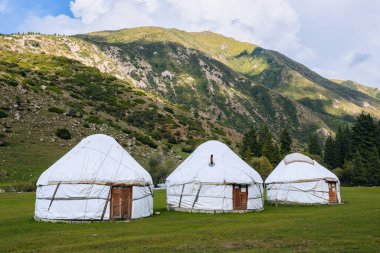Yurt. Kırgızistan ve Asya ülkelerinin ulusal eski evi. Ulusal konut. Yeşil çayırlar ve dağlık arazilerin arka planında yurtlar. Yurt kampı turistler için.