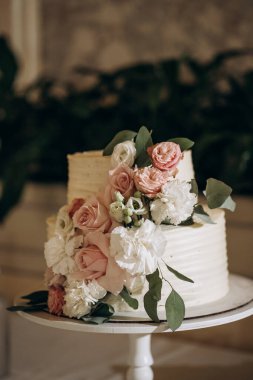 Pembe ve beyaz çiçeklerle süslenmiş beyaz düğün pastası