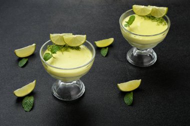 Limon dilimleriyle süslenmiş bir kasede limon kreması. Siyah bir arkaplanda