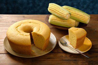 Tahta bir tabakta mısır keki, küçük bir tabakta bir dilim, masada yeşil mısır, mavi arka plan