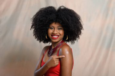 Kolundaki aşı çıkartmasını gösteren afro saçlı güzel bir Afrikalı Amerikalı kadının portresi..