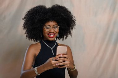 Genç Afrikalı Amerikalı kadın bej arka planda Brezilya parası tutuyor.,