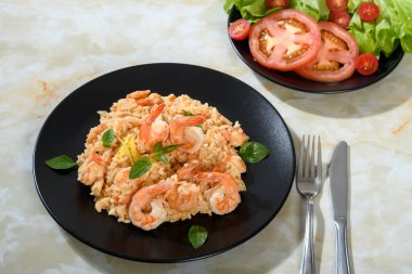 Lezzetli risotto, mermer bir yüzey üzerinde siyah bir tabakta karidesler.