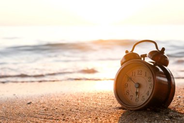 Yeni bir günün sabahı, kumsalın güneş ışığında çalar saat. Sağlık ve tatil kavramı.