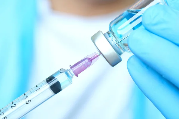 Doktorun elinde hastanede bir şırınga ve mavi bir aşı şişesi var. Sağlık ve tıbbi kavramlar