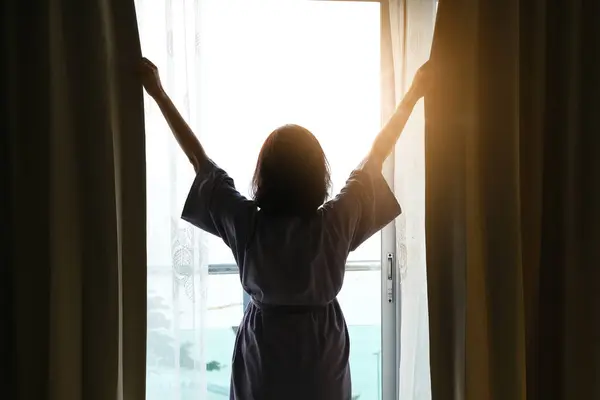 The woman woke up early. She stood at the window in her bedroom and she lifted up both arms to refresh. In the morning
