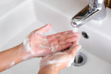 Güzel bir kadının elleri, deriyi yıkamak için ellerini lavaboda köpükle yıkar ve ellerden su akar. Sağlık kavramı, temizlik ve mikropların ellere ve güzelliğe temas etmesini engelleme