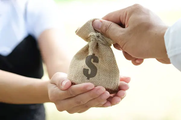 The hand of a businessman gives a bag of dollars to a woman. She picks up the bag from the hand of a businessman. The concept of help and the world economy.