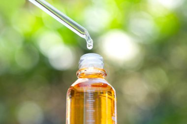 Yüzün serum kolajen nemlendiricisini açık sarı şişe yumuşak ışık arka planına döküyorum. Koruyucu cilt bakımı yüz özü yağı, C vitamini güzellik ve kaplıca konsepti.