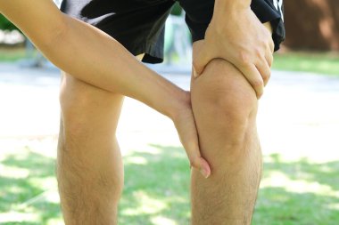 Diz ağrısı. Adam parkta duruyor. Eli dizinden sıkıştı. Acıyı dindirmek için ayaklarının ağrıması ve kaslarının yorulması. sağlık kavramları.