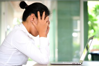 woman sitting down, his face unsettled. At the computer desk she has headaches and stress. Cause of hard work and insufficient rest.