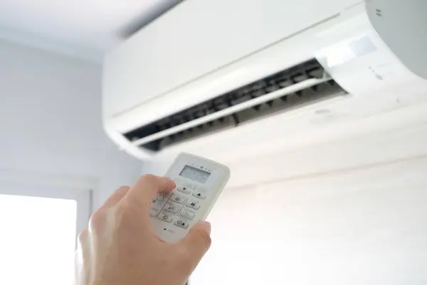 人的手打开遥控器空调机在他的卧室里冷却到25摄氏度 健康概念和节能 免版税图库图片