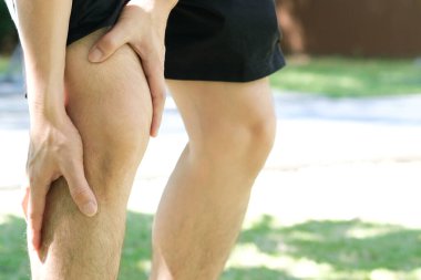 Diz ağrısı. Adam parkta duruyor. Eli dizinden sıkıştı. Acıyı dindirmek için ayaklarının ağrıması ve kaslarının yorulması. sağlık kavramları.