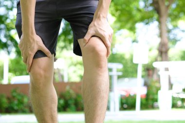 Diz ağrısı. Adam parkta duruyor. Eli dizinden sıkıştı. Acıyı dindirmek için ayaklarının ağrıması ve kaslarının yorulması. sağlık kavramları.