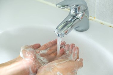 Kadının elleri, deriyi yıkamak için ellerini lavaboda köpükle yıkar ve su ellerinden akar. Sağlık kavramı, temizlik ve mikrop ve koronavirüsün ellerle temas etmesini önlemek