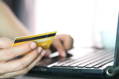 Genç adam oturma odasında oturmuş, bilgisayarını kullanmış ve internetten mal almak için ona kredi kartı tutuyormuş.