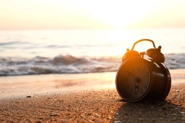 Yeni bir günün sabahı, kumsalın güneş ışığında çalar saat. Sağlık kavramı.