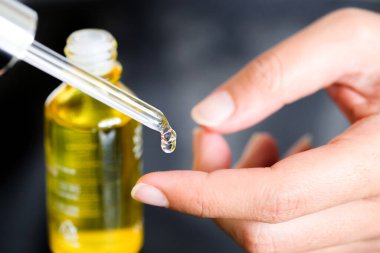 Güzel bir kadının elleri, yüzüne serum kolajen nemlendirici dökerek berrak sarı şişe yumuşak ışık arka planına döküyor. Koruyucu cilt bakımı yüz özü yağı, C vitamini güzellik ve kaplıca konsepti.