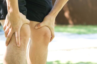 Diz ağrısı. Adam parkta duruyor. Eli dizinden sıkıştı. Acıyı dindirmek için ayaklarının ağrıması ve kaslarının yorulması. sağlık kavramları.