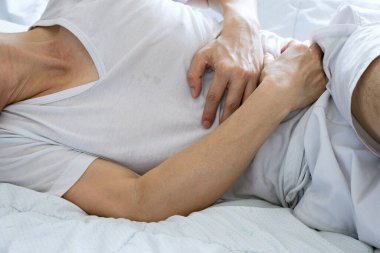 Genç adam karnını tutmak için ellerini kullanıyor ve karnı ağrıyor. İzole edilmiş beyaz arka planda.