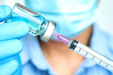 Doktorun elinde hastanede bir şırınga ve mavi bir aşı şişesi var. Sağlık ve tıbbi kavramlar.