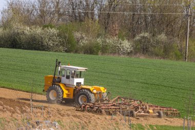 İlkbaharın başlarında bir traktör tohum ekme makinesiyle tarlayı sürüyor..