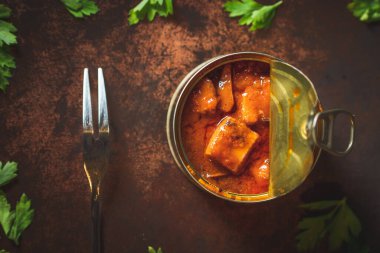 Canned octopus with american sauce open on a dark brown table witha fork and parsley. Ready for eat. 
