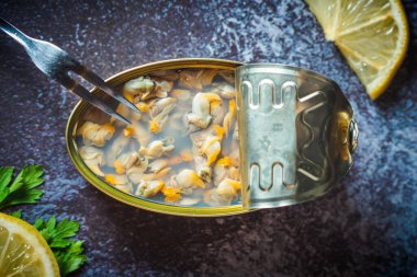 Canned cockles open on a dark blue table with a fork, lemon and parsley. Ready for eat.  clipart