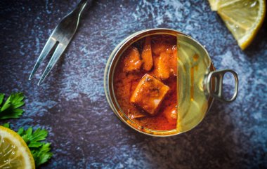 Canned octopus with american sauce open on a dark blue table with a fork, lemon and parsley. Ready for eat. 