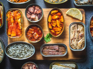 Konserveleri farklı ürünlerle, balık ve deniz ürünleriyle, doğal ya da turşulu, ahşap kesim tahtası ve limonla karanlık bir masada muhafaza edin. Yemek hazır..