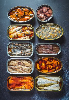 Farklı ürünlerin olduğu konserveleri muhafaza edin, balık ve deniz ürünleri, doğal ya da turşulu, karanlık bir masada açık. Yemek hazır..