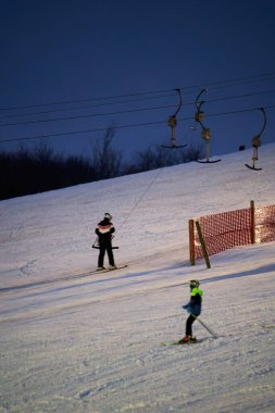Treffelhausen, Germany - January 28, 2022: Ski drag lift in operation at night with lighting. Winter athletes on the slopes in the snow. Long exposure, blurred.