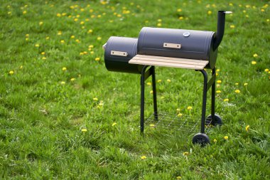 New smoker barbecue grill. Equipment for cooking and smoking. Meadow with dandelions in the background. High angle view.