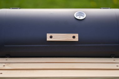 New smoker barbecue grill. Equipment for cooking and smoking. Wooden shelf and handle. Closeup.