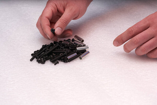 2 hands searching black screw on a bolt heap. Connecting elements for industry and crafts.